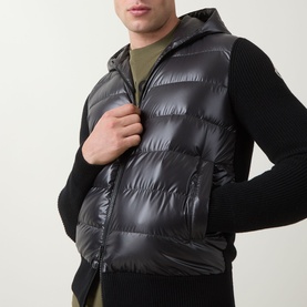 Model wearing Moncler black quilted gilet with hood over a dark knit cardigan, styled with khaki base layer