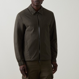 Model wearing Moncler Caramantran Down Overshirt in dark green with zip closure, collar, long sleeves, and elastic cuffs, styled with khaki trousers.
