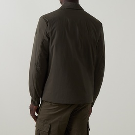 Model wearing Moncler Caramantran Down Overshirt in dark green, back view, showing zip closure and elastic cuffs, styled with cargo trousers.