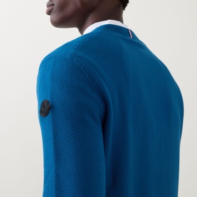 Model wearing Moncler navy cotton crew neck knit, showing sleeve badge logo detail, styled with a white collared shirt underneath.