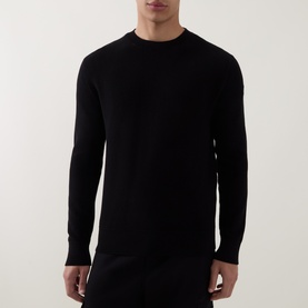 Model wearing black crew neck long sleeve knit jumper with ribbed cuffs and hem, styled with black trousers
