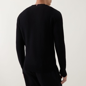 Model wearing black long-sleeve crewneck knit top, rear view, styled with black trousers, small branded label visible at neckline.