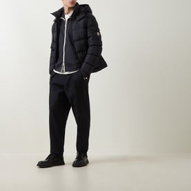 Model wearing Moncler navy down jacket with hood, styled with black tapered trousers and black boots.
