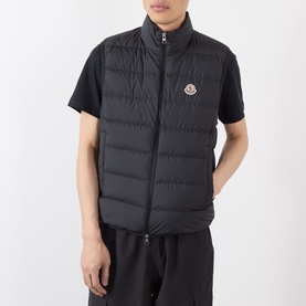 Model wearing Moncler Contrin Down Gilet in black, sleeveless quilted design with logo patch, styled with black T-shirt and trousers.