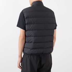 Model wearing Moncler Contrin Down Gilet in black, rear view, styled with black T-shirt and trousers. Quilted sleeveless design visible.