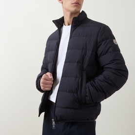 Model wearing Moncler navy quilted down jacket with funnel neck and logo badge, styled with white T-shirt and navy trousers