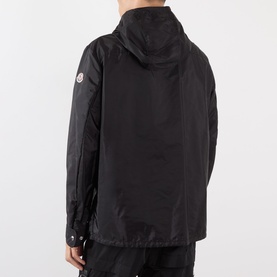 Model wearing Moncler black hooded jacket, rear view, lightweight polyamide shell with logo badge on sleeve, worn with black trousers