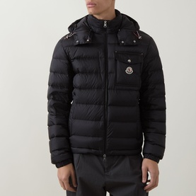 Model wearing Moncler black quilted down jacket with detachable hood, chest pocket, and gold-tone zip detailing.