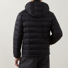 Model wearing Moncler black quilted down jacket, rear view, with attached hood and ribbed side panels, styled with dark joggers.