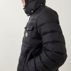 Model wearing Moncler black quilted down puffer jacket with chest flap pocket, hood, and logo badge patch