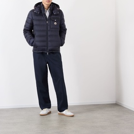 Model wearing Moncler dark blue quilted hooded down jacket, styled with navy trousers and white trainers.
