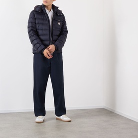 Model wearing Moncler dark blue quilted down jacket with hood, styled with navy trousers and white loafers.