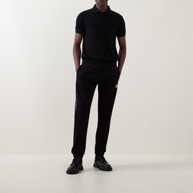 Model wearing Moncler black cotton polo shirt, styled with matching black joggers and black leather shoes.