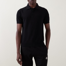 Model wearing Moncler black cotton polo shirt with three-button placket and logo badge, paired with black trousers.