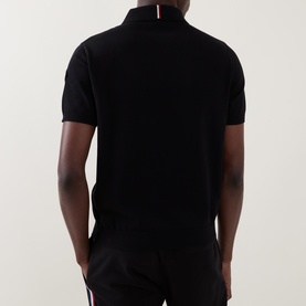 Model wearing Moncler black cotton polo shirt, back view, with red and white stripe collar detail.