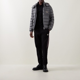 Model wearing Moncler black cotton polo, styled with grey quilted down jacket and black joggers with side stripe detail.