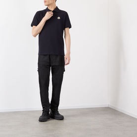 Model wearing Moncler blue cotton polo shirt with logo badge, styled with black cargo trousers and black boots.