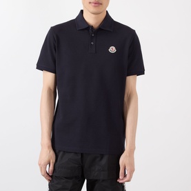 Model wearing Moncler blue cotton polo shirt with logo badge patch, short sleeves, and three-button placket