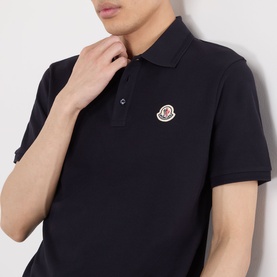 Model wearing Moncler blue cotton polo shirt with signature logo badge on chest, short sleeves and ribbed collar