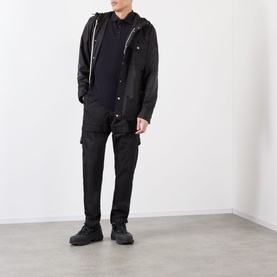 Model wearing Moncler blue cotton polo, styled with black hooded jacket, black cargo trousers and black trainers.