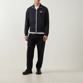 Model wearing Moncler dark blue zip-through sweatshirt with white trim and logo patch, styled with black joggers and black shoes