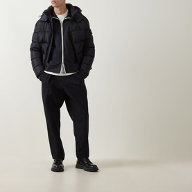 Model wearing Moncler dark blue sweatshirt layered under a black quilted hooded jacket, with dark tapered trousers and black leather shoes.