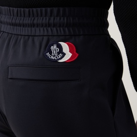 Moncler dark blue sweatpants close-up, featuring tricolour logo patch on hip and side contrast stripe detail.