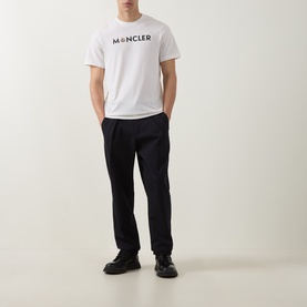Model wearing Moncler natural cotton T-shirt with chest logo print, styled with black tailored trousers and black shoes.