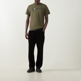 Model wearing Moncler dark green cotton T-shirt with chest logo print, styled with black trousers and dark trainers.