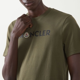 Model wearing Moncler dark green cotton T-shirt with embroidered logo lettering and badge detail on chest, close-up view.