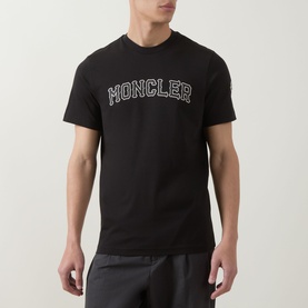 Model wearing Moncler black cotton T-shirt with white arched logo lettering on chest and small arm badge.