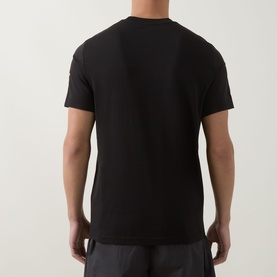 Model wearing Moncler black cotton T-shirt, rear view, styled with dark grey trousers.