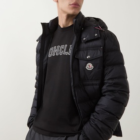 Model wearing Moncler black cotton T-shirt with logo print, styled with a black quilted hooded down jacket.