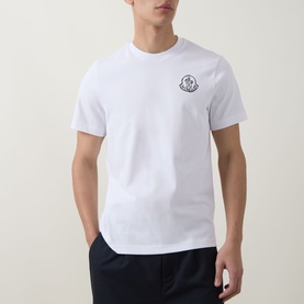 Model wearing Moncler white cotton T-shirt with small logo badge on chest, styled with dark navy trousers.