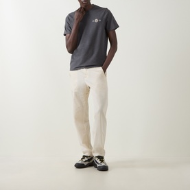 Model wearing Moncler dark grey cotton T-shirt with chest logo, styled with cream trousers and black trail sneakers.