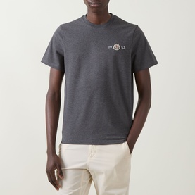 Model wearing Moncler dark grey cotton T-shirt with small chest logo badge, styled with cream trousers.