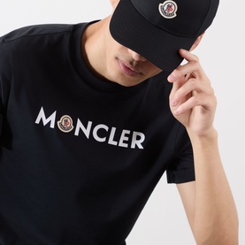 Model wearing Moncler Felt Logo Graphic T-Shirt in navy with chest logo lettering, styled with a black Moncler cap.