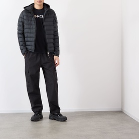 Model wearing Moncler Felt Logo Graphic T-Shirt in navy, styled with a dark quilted jacket, black trousers and chunky trainers.