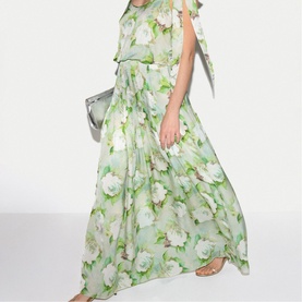 Model wearing Jigsaw green floral maxi dress with flutter sleeves, styled with strappy sandals and silver clutch bag
