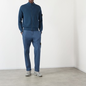 Model wearing blue zip-up knit cardigan with badge patch, styled with matching blue trousers and grey trainers