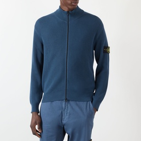 Model wearing teal blue Stone Island zip-through knit cardigan with arm badge, styled with light blue trousers.
