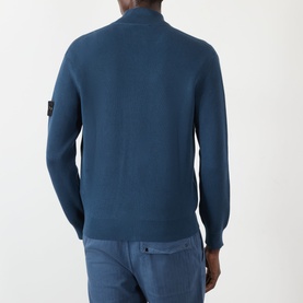 Model wearing a teal blue fine-knit zip-neck sweater with Stone Island badge on left sleeve, styled with light blue trousers.