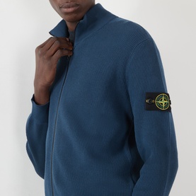 Model wearing teal ribbed zip-through knit cardigan with Stone Island badge patch on left sleeve, zipping up collar