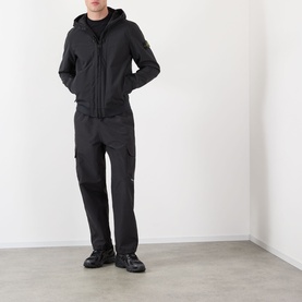 Model wearing Stone Island Soft Shell-R-e.dye&reg; Wind Resistant Jacket in black, styled with matching black cargo trousers and black shoes.