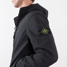 Model wearing Stone Island Soft Shell-R-e.dye&reg; Wind Resistant Jacket in black, showing compass logo badge on left sleeve and hood detail.