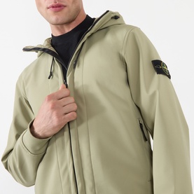 Model wearing Stone Island Softshell-R_e.dye&reg; Wind Resistant Jacket in laurel green, with drawstring hood and logo patch on left sleeve.