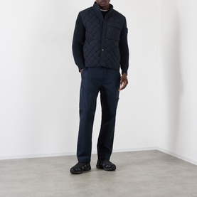 Model wearing Stone Island blue quilted casual jacket with chest pockets, styled with navy trousers and black chunky boots.