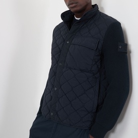Model wearing Stone Island blue quilted casual jacket with knit sleeves, chest pockets, and signature arm badge detail.
