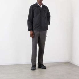 Model wearing Stone Island black casual jacket with chest badge, styled with grey trousers and black shoes.