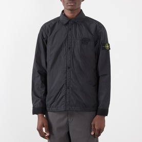 Model wearing Stone Island black nylon casual jacket with signature compass badge, chest pocket, and snap button placket, styled with grey trousers